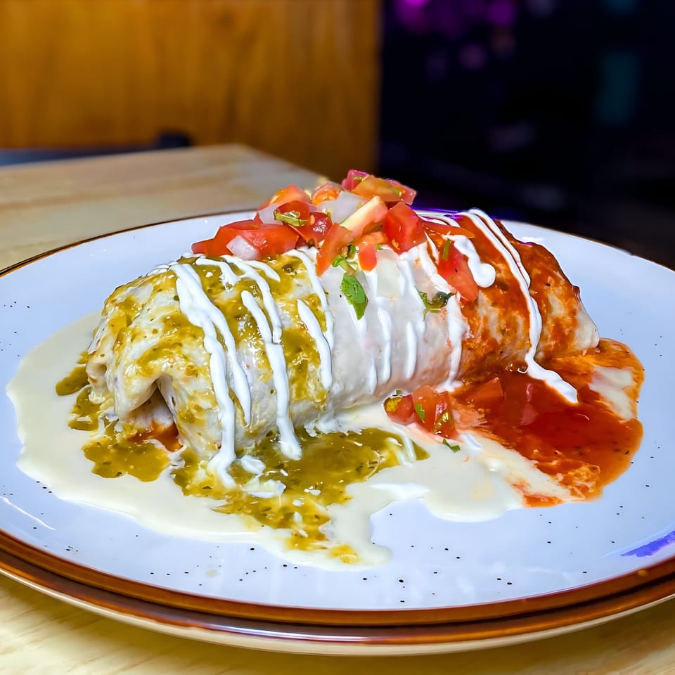 A large La Costa Mexican cantina burrito covered in green and red sauce, sour cream, and pico de gallo.