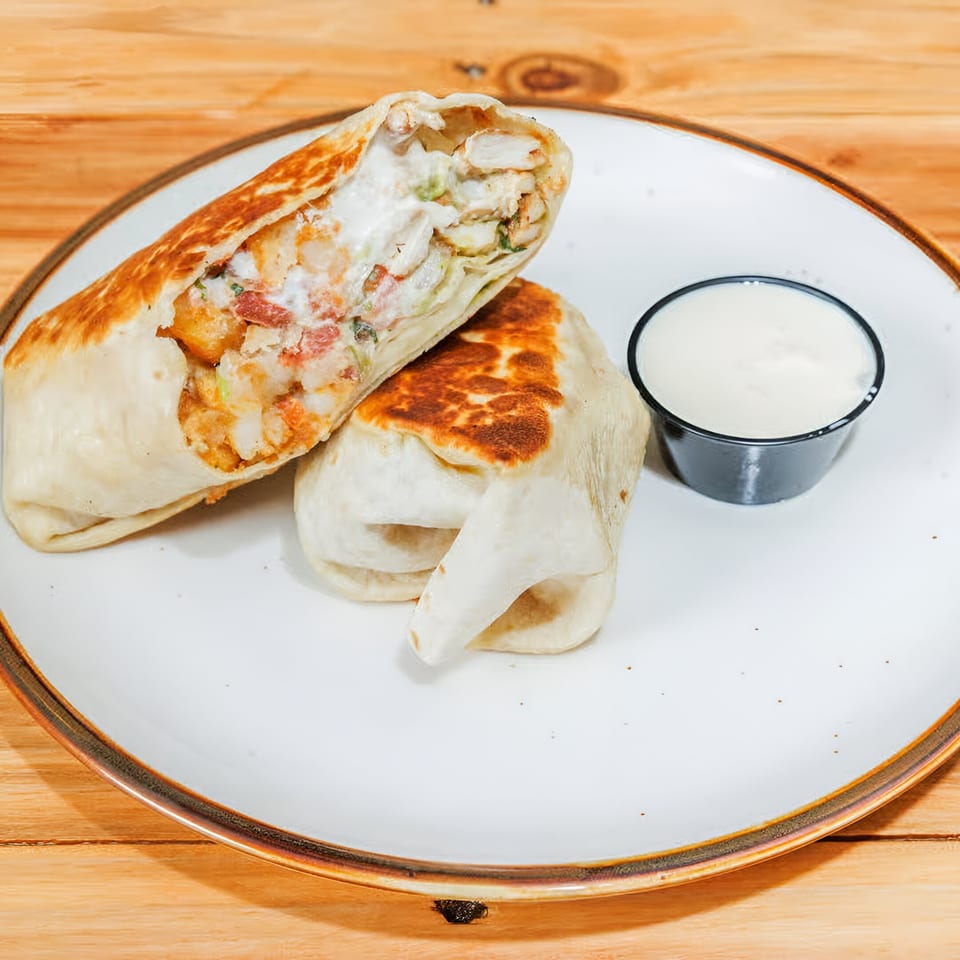Two La Costa Mexican cantina burritos, one cut open to show filling, with a side of white sauce.