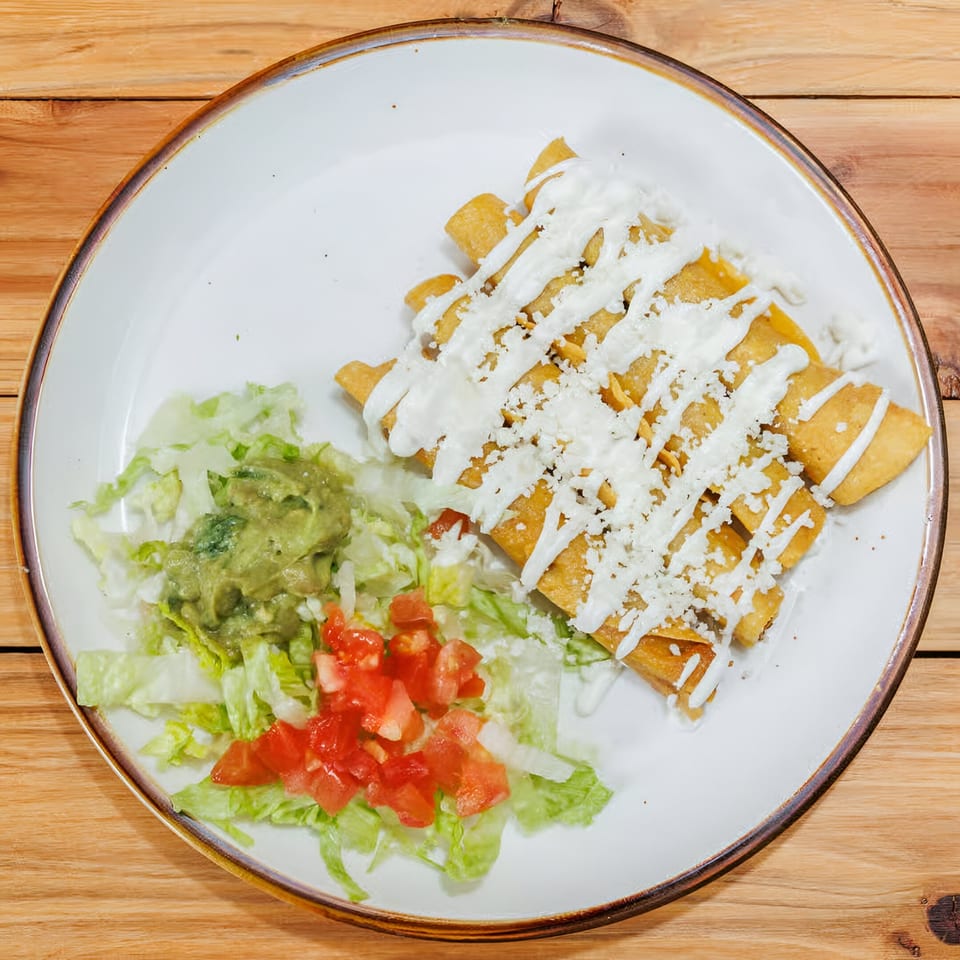 Golden taquitos drizzled with crema and cheese, served with guacamole, lettuce, and diced tomatoes.
