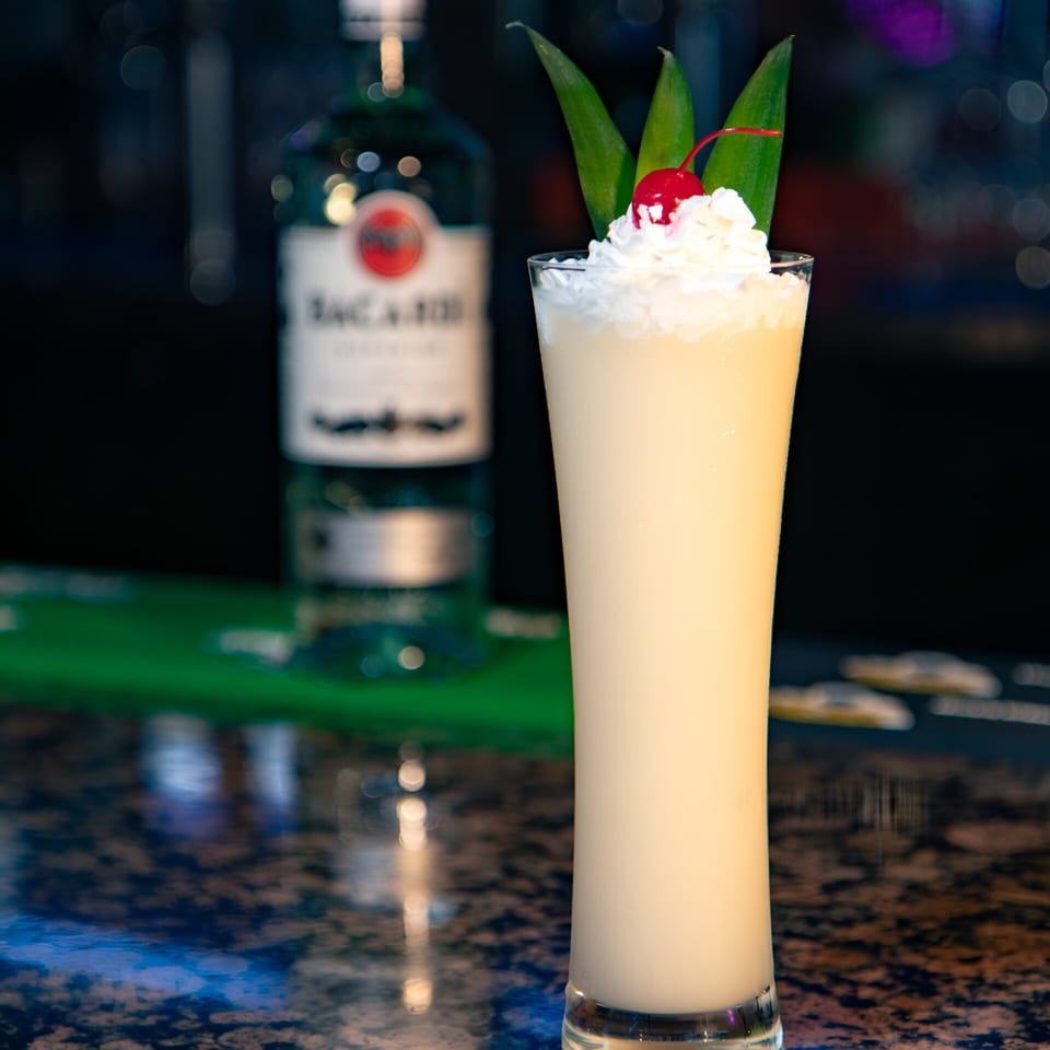 A tall glass of creamy piña colada with whipped cream, a cherry, and pineapple leaves.