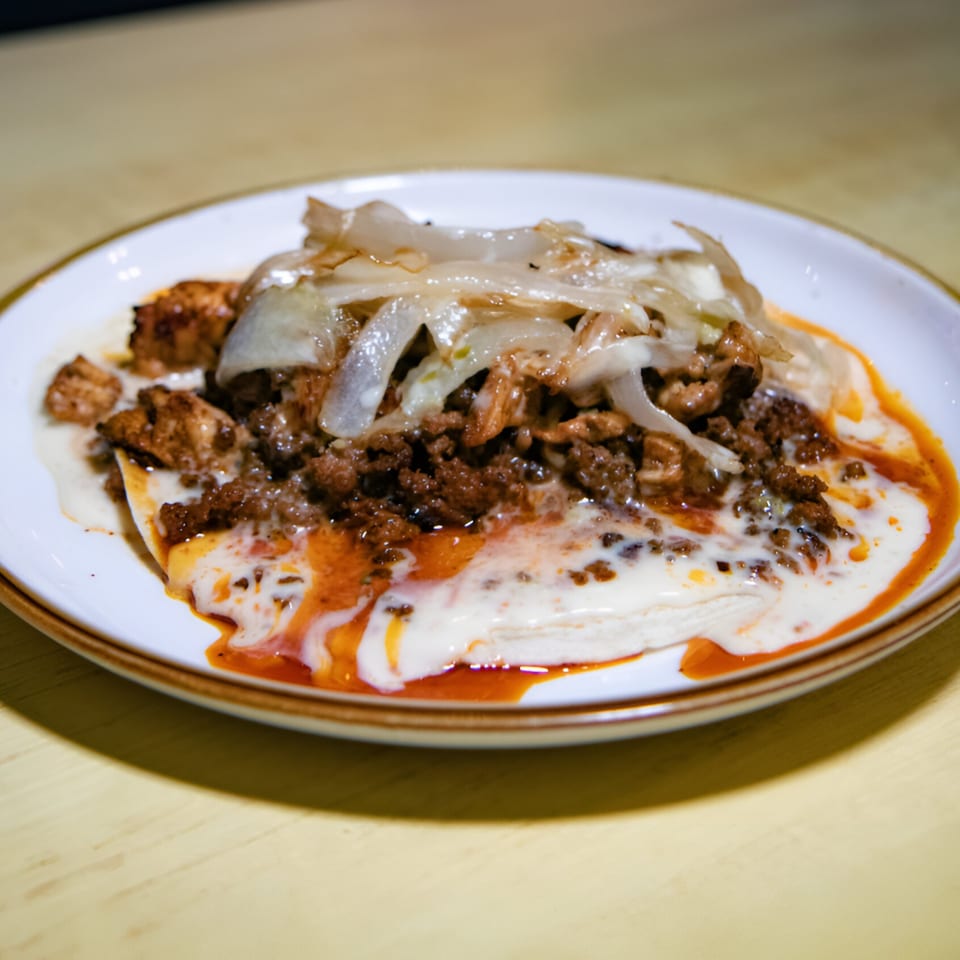 La Costa Mexican cantina's dish with ground meat, chicken, onions, and white sauce on a plate.