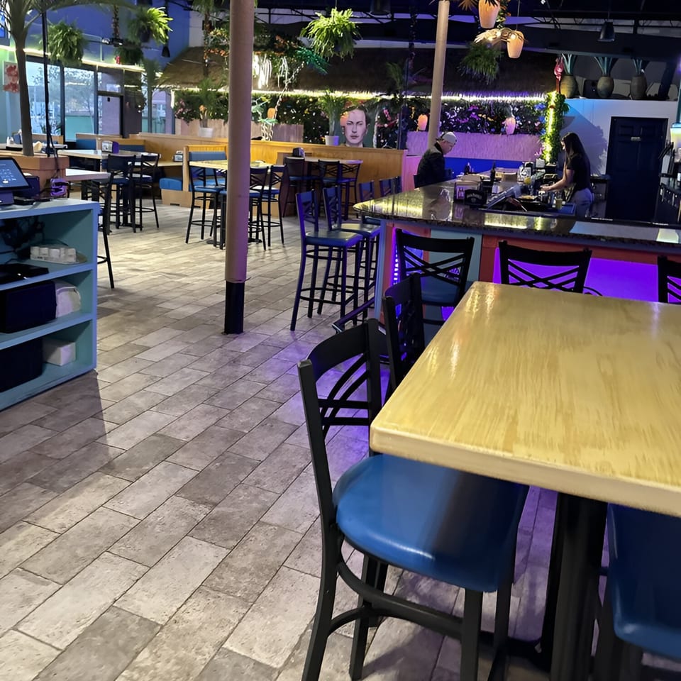 Interior of La Costa Mexican cantina with blue chairs, high tables, and a bar with purple lighting.