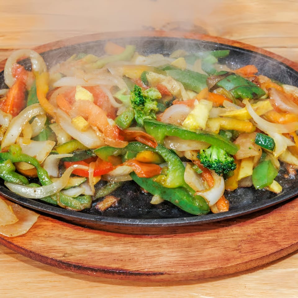 Sizzling La Costa fajita vegetables, including onions, bell peppers, broccoli, and carrots, on a hot plate.