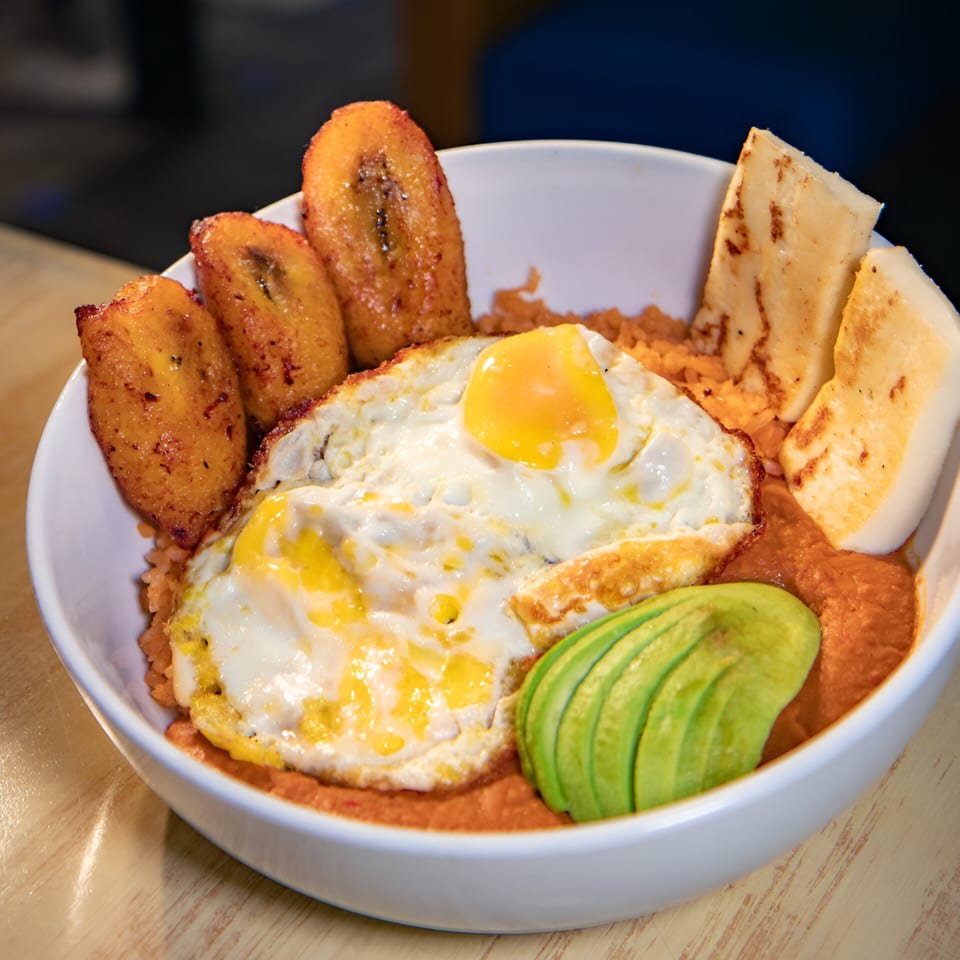 Mexican breakfast bowl with fried eggs, plantains, avocado, and cheese in a white bowl.
