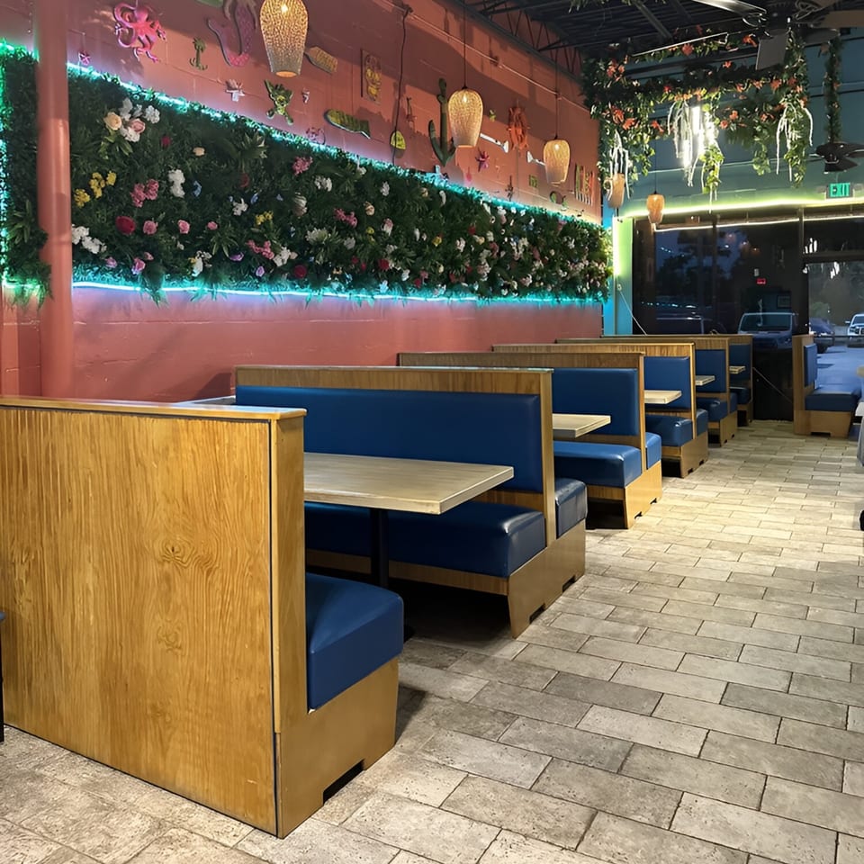 La Costa Mexican cantina interior with blue booths, wooden tables, and a floral wall with neon lights.
